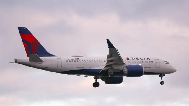 A white Delta Air Lines jet with a red and blue tail flying low under a pink cloudy sky