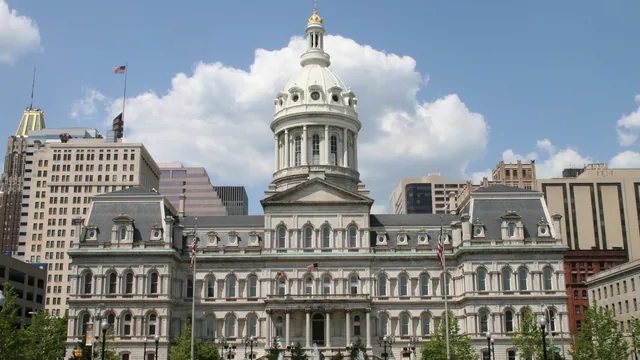 Historic Baltimore City Hall with its white dome and clock tower rising above a tree-lined plaza