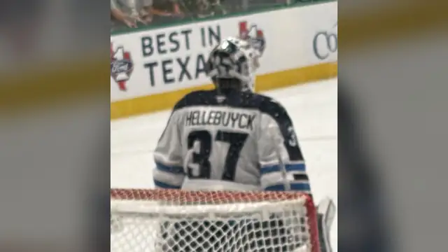 Goaltender Connor Hellebuyck in his white No. 37 Winnipeg Jets jersey and mask standing in the crease during an April 2026 game in Dallas