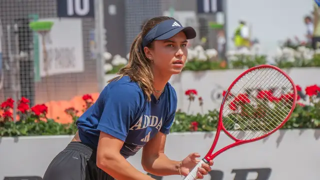 Iva Jovic in a navy visor and shirt waits to return serve on a clay court in Rome