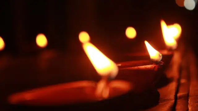 A row of clay diya lamps burns with bright flames in the dark for Diwali