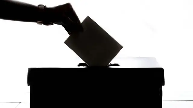Close view of a person's hand marking a paper election ballot with a blue pen