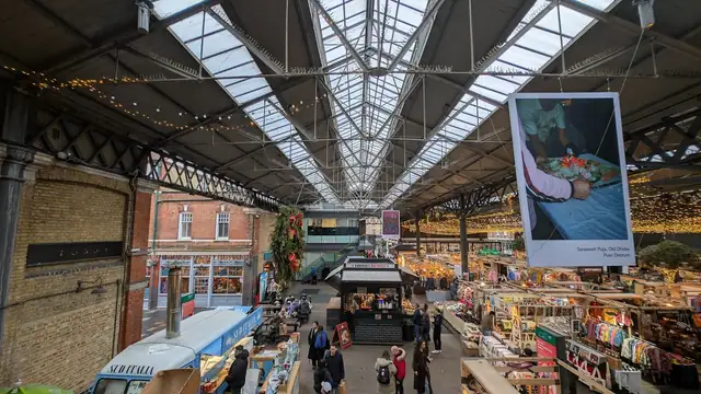 Shoppers walk beneath the tall glass and steel roof of Old Spitalfields Market in east London past food stalls and hanging banners