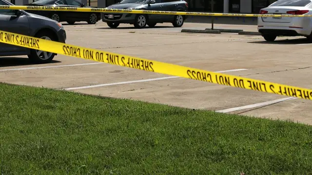Yellow crime scene tape stretched across a parking lot with cars parked behind it