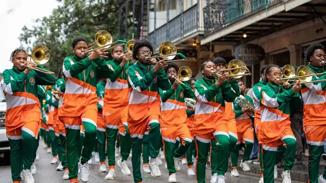 Young trombone players in bright orange and green uniforms march down a city street playing their horns during a parade