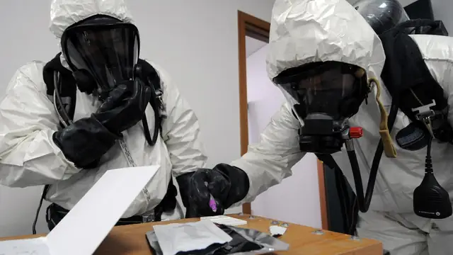 Emergency responders in white hazmat suits and breathing masks test a white powder from a suspicious letter on a wooden table