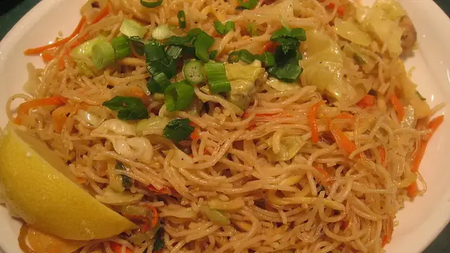A plate of pancit, Filipino stir-fried noodles, topped with green onions and served with lemon