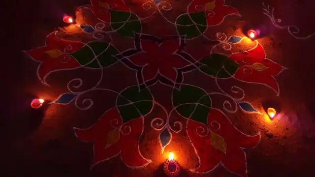A red and green rangoli pattern glows with small flickering diya lamps placed around it