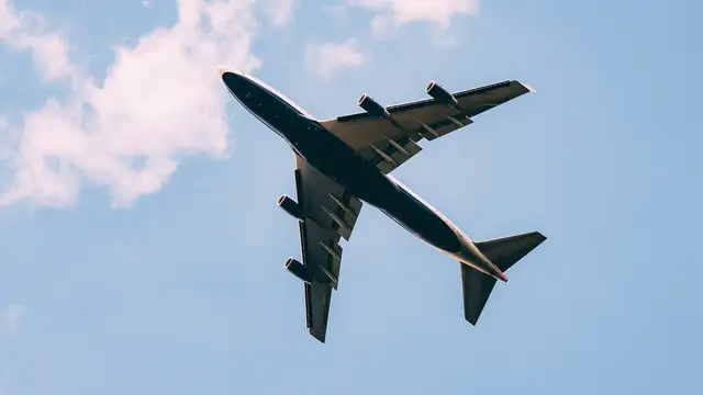 A passenger jet seen from below as it flies across a blue sky with scattered clouds