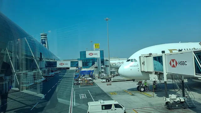 A passenger jet parked at a jet bridge beside the glass terminal at Dubai International Airport