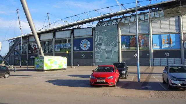 The Etihad Stadium in Manchester with the Manchester City crest on its outer wall on a sunny day