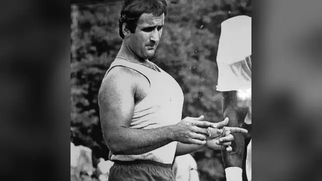 A young Chuck Amato in a white sleeveless shirt shows a player a technique with his hands in an old black-and-white photo