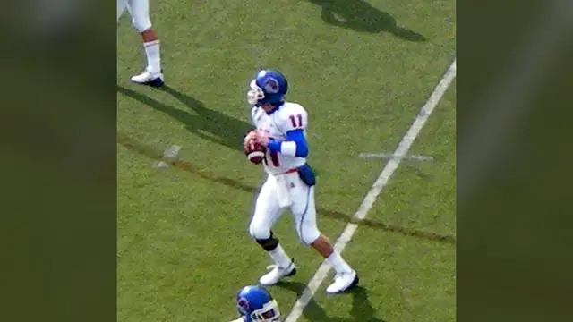 Kellen Moore in a white Boise State No. 11 jersey and blue helmet holds a football during pregame warmups at Nevada in 2008