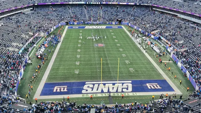A wide view of a packed MetLife Stadium with the Giants logo painted at midfield