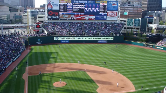 Progressive Field in Cleveland with green seats and the scoreboard rising above the outfield on a sunny day
