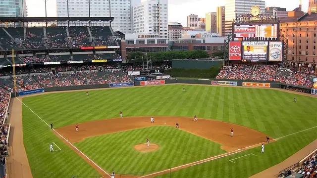 A crowded modern ballpark seen from the upper deck with city towers beyond the outfield