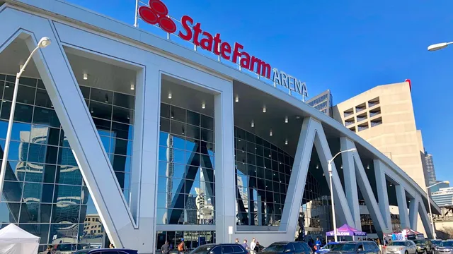 Exterior of State Farm Arena in Atlanta with glass walls and a curved roof under a blue sky