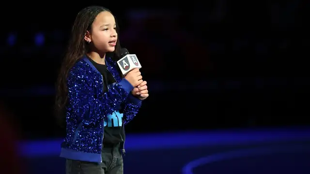 Young singer Heiress Harris in a sparkling blue sequin jacket holding an Atlanta Dream microphone as she sings on an arena floor