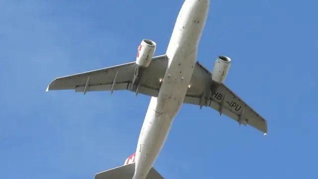 A white passenger jet climbs overhead against a clear blue sky just after takeoff with its landing gear still down