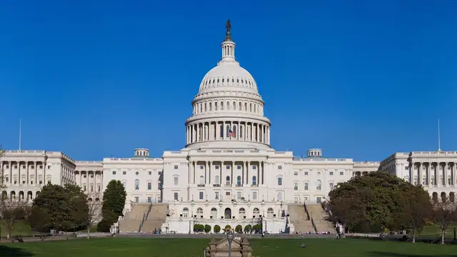 The west front of the United States Capitol with its white dome rising over green lawns under a clear blue sky