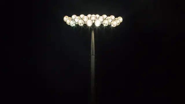 A bank of stadium floodlights glows against a black night sky