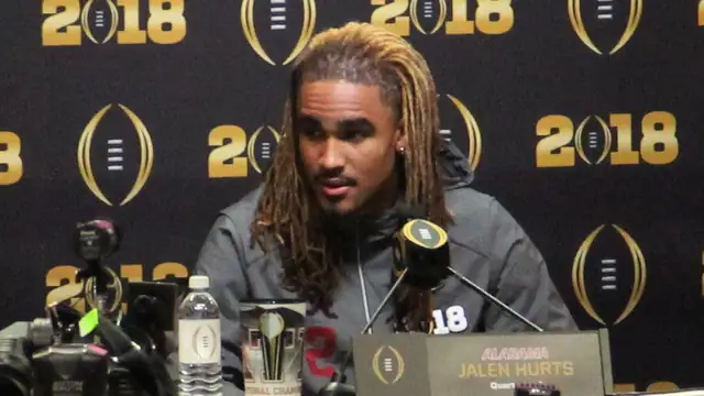 Jalen Hurts, then an Alabama quarterback, answers questions behind an Alabama nameplate at a College Football Playoff media day podium in January 2018