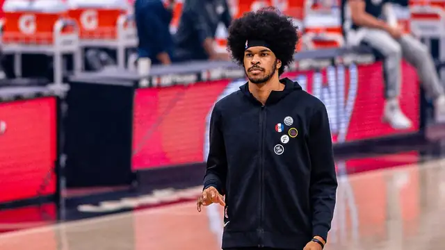 Jarrett Allen in a black Cleveland Cavaliers warmup jacket and headband walks across the court before a game