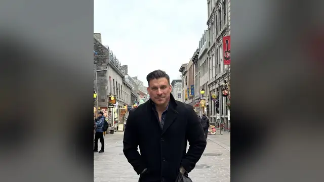 Jax Taylor in a dark coat standing on a cobblestone street
