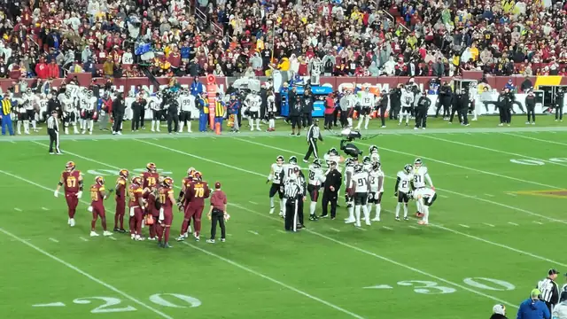 Washington Commanders players in burgundy jerseys gather on the field during a home game while opposing players huddle nearby