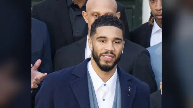 Celtics star Jayson Tatum in a navy suit stands with teammates at the White House championship celebration