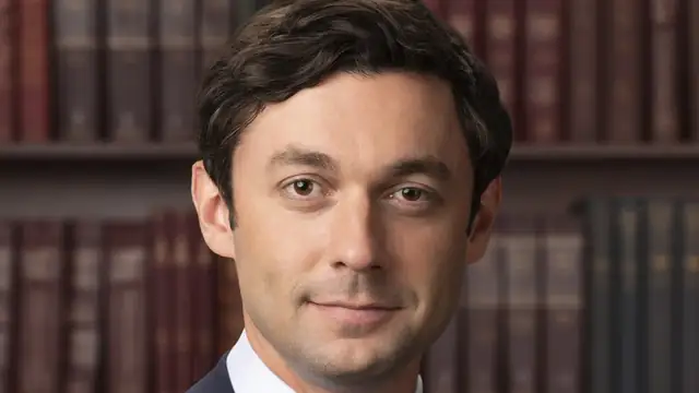 Official US Senate portrait of Georgia Sen. Jon Ossoff smiling in front of shelves of law books