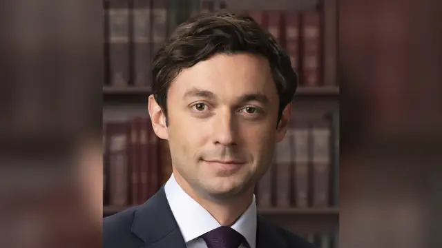 Official Senate portrait of Jon Ossoff in a dark suit and purple tie in front of shelves of law books