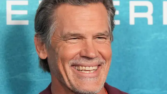 Josh Brolin smiling in a maroon blazer at a movie premiere backdrop