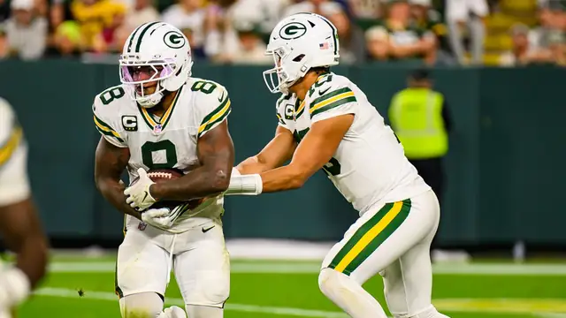 Josh Jacobs taking a handoff in a white Green Bay Packers uniform at Lambeau Field