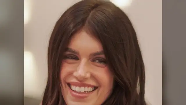 Kaia Gerber smiling with long brown hair against a soft beige background
