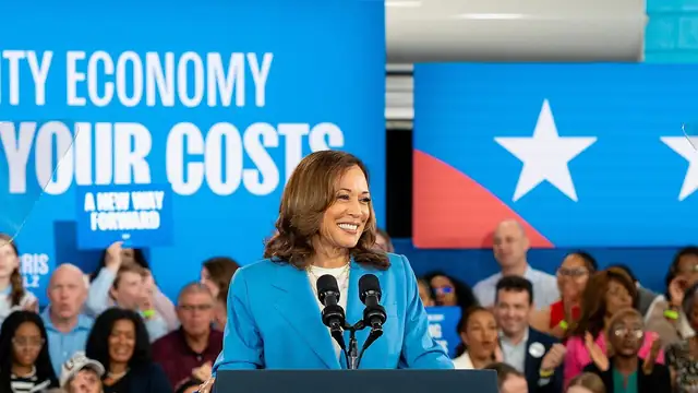 Kamala Harris smiles while speaking at a podium with the vice presidential seal in front of a cheering crowd at a 2024 campaign rally