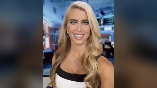 Katie Zacharia smiling with long blonde hair in a black and white top inside a TV studio
