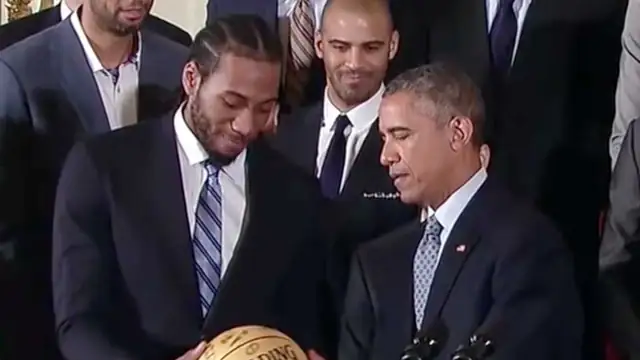 Kawhi Leonard in a suit handing a basketball to President Barack Obama at the Spurs' 2015 White House visit