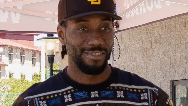 Kawhi Leonard in a dark patterned sweater and a brown cap stands outdoors during a daytime visit
