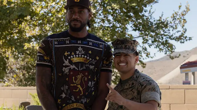Kawhi Leonard in a cap and a patterned black shirt stands beside a smiling Marine during a 2022 visit to Camp Pendleton