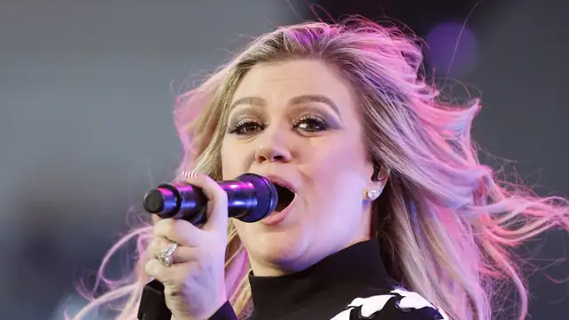 Kelly Clarkson singing into a microphone onstage with her hair blowing