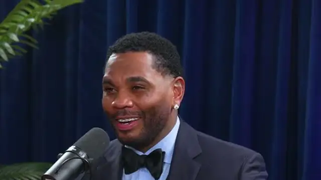 Kevin Gates smiling in a tuxedo and bow tie during a podcast interview