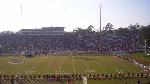 A marching band stands in formation on the field at Bragg Memorial Stadium in front of packed stands