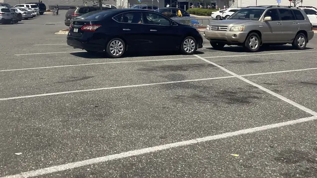 A black sedan and a gold SUV parked in a sunny store parking lot