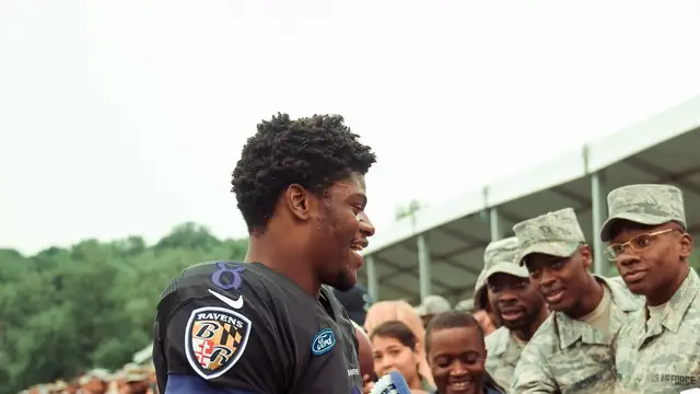 Smiling Baltimore Ravens quarterback Lamar Jackson in a black Ravens practice jersey greets service members at training camp