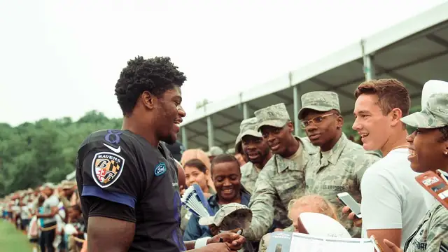 Baltimore Ravens quarterback Lamar Jackson smiles while signing autographs for service members at Ravens training camp in 2018