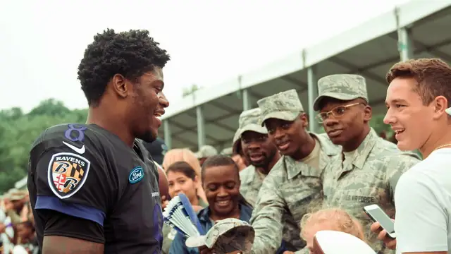Lamar Jackson in a black Ravens jersey smiles while greeting Air Force service members and fans at Ravens training camp