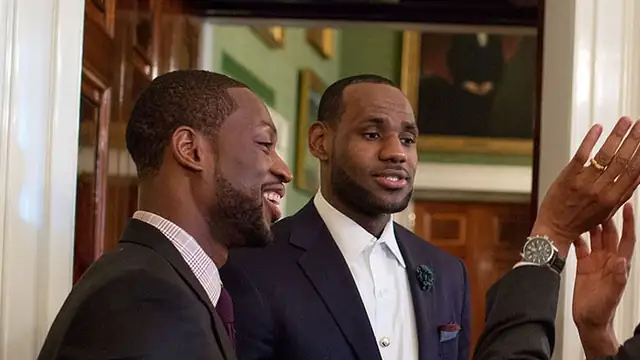 Dwyane Wade and LeBron James in dark suits smile together in a reception room at the White House