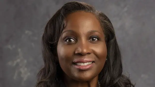 Official Federal Reserve portrait of Gov. Lisa Cook smiling in a dark jacket and pearl necklace against a gray backdrop