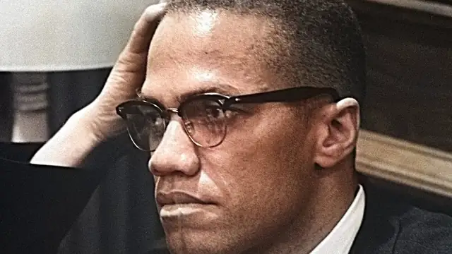 Black-and-white portrait of Malcolm X in glasses resting his head on his hand during a 1964 interview